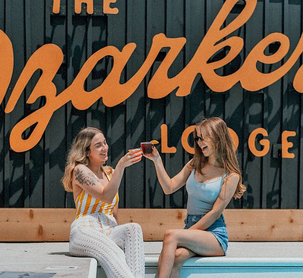 Two women toasting cocktails by the pool at The Ozarker.