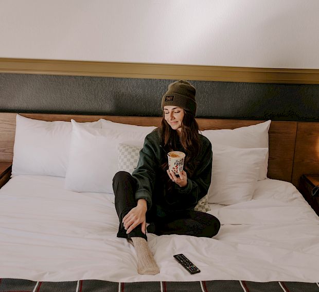 A woman wearing sweats having coffee in bed at The Ozarker Lodge.