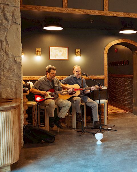 Two men playing guitars in a hotel lobby.