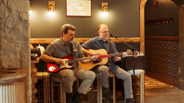 Two men playing guitars in a hotel lobby.