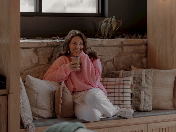 A woman in a pink sweatshirt drinking an iced coffee.
