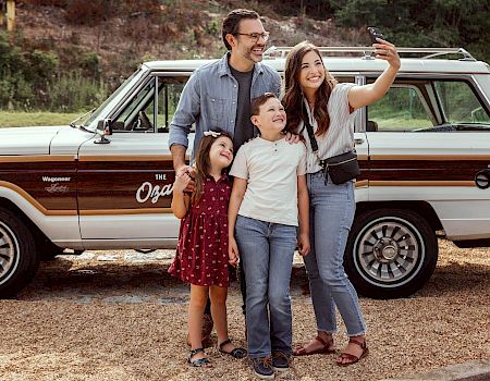 A family of four posing for a photo in front of a car.
