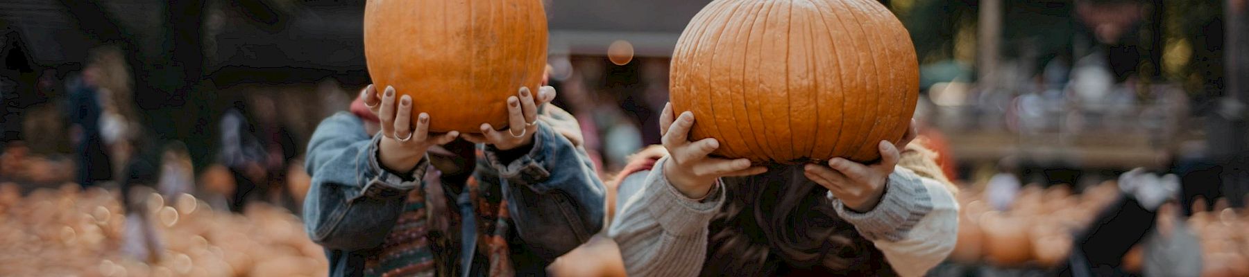 Two women holding up pumpkins to cover their faces.