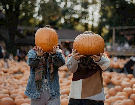 Two women holding up pumpkins to cover their faces.